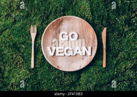 Stoviglie monouso in legno di materiali naturali con Word GO VEGAN, cucchiaio di legno, forchetta su fondo muschio verde. Stile di vita sostenibile ed ecologico Foto Stock
