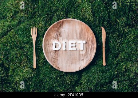 Stoviglie monouso in legno di materiali naturali con dieta a parole, cucchiaio di legno, forchetta su fondo di muschio verde. Stile di vita sostenibile ed ecologico Foto Stock
