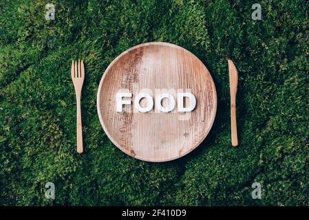 Stoviglie monouso in legno di materiali naturali con PEZZE ALIMENTARI, cucchiaio di legno, forchetta su fondo di muschio verde. Stile di vita sostenibile ed ecologico Foto Stock