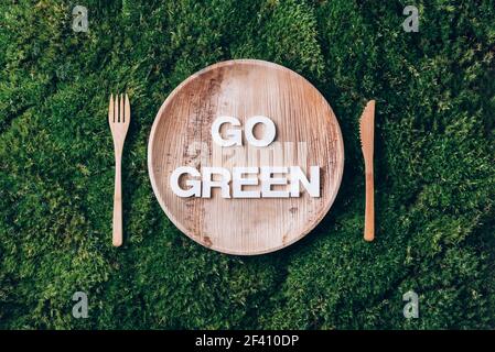 Stoviglie monouso in legno di materiali naturali con parola GO VERDE, cucchiaio di legno, forchetta su fondo muschio verde. Stile di vita sostenibile ed ecologico Foto Stock