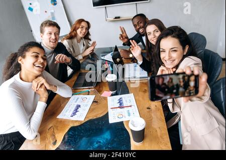 Felice gente di affari che fa selfie di gruppo sulla riunione di briefing, sorridente. I colleghi più sicuri hanno concluso le trattative con successo, godendo dei risultati del lavoro, del concetto di partnership Foto Stock