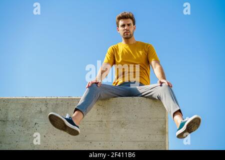 Giovane uomo seduto su una sporgenza che guarda intorno. Uomo seduto su una sporgenza che guarda intorno Foto Stock