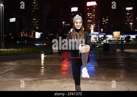 Giovane donna che allunga le gambe come un pre-workout e godendosi una bella serata piovosa in una grande città Foto Stock