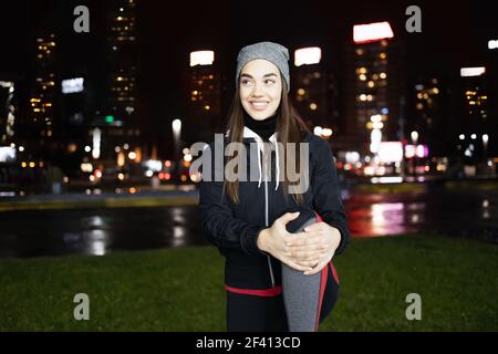 Giovane donna che allunga le gambe come un pre-workout e godendosi una bella serata piovosa in una grande città Foto Stock