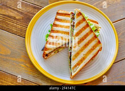 Panino panino integrale di pollo e avocado, triangoli sopra la vista su un tavolo di legno. Panino di pollo e avocado integrale sopra la vista Foto Stock