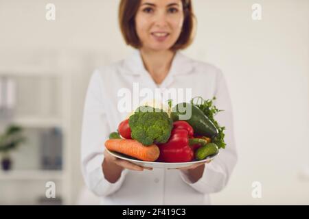 Primo piano di un piatto di verdure fresche che una giovane nutrizionista femminile sta tenendo davanti a lei. Foto Stock