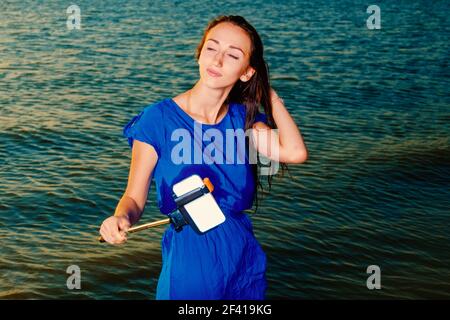 Gli occhi chiusi una donna fanno selfie utilizzando selfie stick nella parte anteriore di mare verde acqua Foto Stock