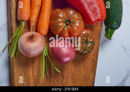 Vari verdi e verdure su tavola da cucina in legno una superficie di marmo bianco. Carote, peperoni, zucchine, pomodori e cipolle Foto Stock