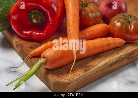 Vari verdi e verdure su tavola da cucina in legno una superficie di marmo bianco. Carote, peperoni, zucchine, pomodori e cipolle Foto Stock