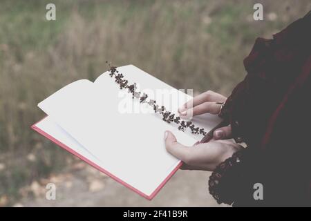 Una giovane donna tiene un diario aperto in cui è incorporato un filo d'erba. Atmosfera retrò in autunno. La nostalgia è un'immagine tonica in natura. Una giovane donna tiene un diario aperto in cui è incorporato un filo d'erba. Atmosfera retrò Foto Stock