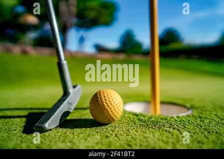 Mini Golf sfera gialla con un bat in prossimità del foro al tramonto Foto Stock