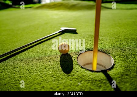 Mini Golf sfera gialla con un bat in prossimità del foro al tramonto Foto Stock