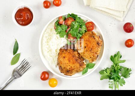 Cosce di pollo fritte con verdure e riso in piatto su fondo di pietra bianca. Vista dall'alto, disposizione piatta Foto Stock