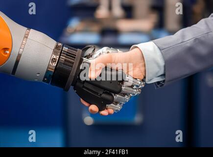 La mano di un uomo d'affari che stringono le mani con un robot androide. Il concetto di interazione umana con intelligenza artificiale. Foto Stock