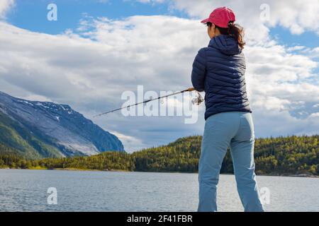 Donna che pesca sulla canna da pesca che gira in Norvegia. La pesca in Norvegia è un modo per abbracciare lo stile di vita locale. Innumerevoli laghi e fiumi e una costa estesa significa opportunità eccezionali... Foto Stock