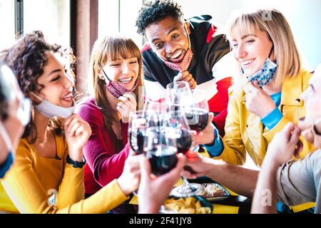 Amici multirazziali che tostano vino rosso al bar del ristorante che indossa l'ambiente aperto Maschera facciale - nuovo concetto di stile di vita normale con felice persone che si divertono insieme Foto Stock