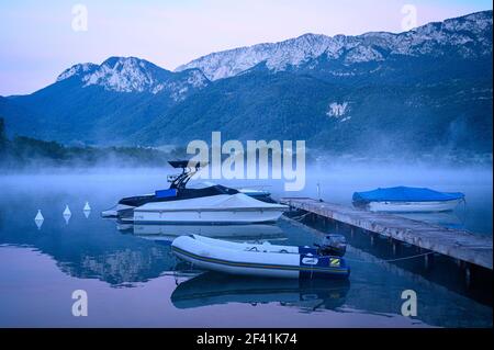 Barche su un tranquillo lago di montagna con nebbia misteriosa (Lago di Annecy) Foto Stock