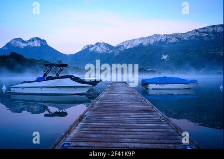 Molo vuoto in legno con barche a motore su un tranquillo lago di montagna Al mattino (Lago di Annecy) Foto Stock