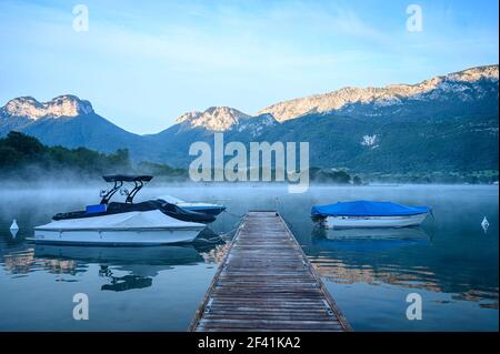 Barche a motore presso il tranquillo molo del lago di mattina circondato da montagne (Lago di Annecy) Foto Stock