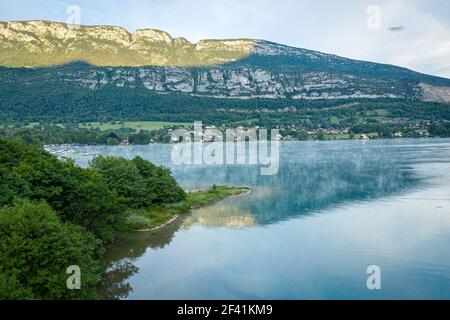 Piccola città sotto una montagna vicino ad un lago coperto Nebbia in Francia Foto Stock