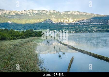 Misterioso lago foggy con piccola città sotto una montagna in lo sfondo Foto Stock