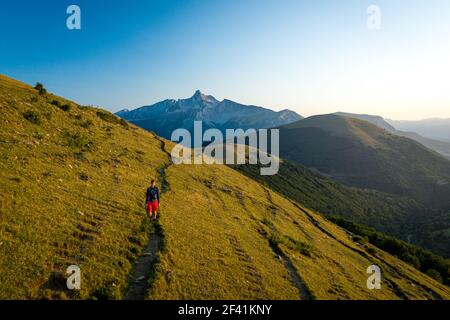 Vista frontale di una persona che camminano su un sentiero di montagna attraverso colline erbose Foto Stock