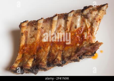 Vista dall'alto delle costolette di maiale al forno immerse in una salsa piccante su sfondo bianco. Gustose ricette di carne fatte in casa. Foto Stock