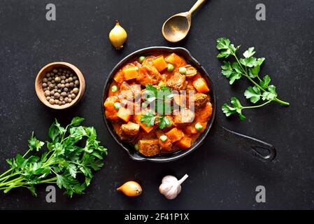 Stufato di manzo con patate e carote in salsa di pomodoro su fondo nero. Vista dall'alto, disposizione piatta Foto Stock