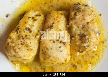 Vista dall'alto di tre gustosi lombi di nasello in salsa verde su un piatto bianco. Pesce e cibo sano. Foto Stock