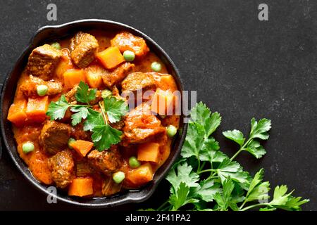 Stufato di manzo con patate e carote in salsa di pomodoro su fondo nero. Vista dall'alto, disposizione piatta Foto Stock