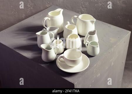 Set di vasetti per latte vuoti o di creme. Stoviglie da cucina e stoviglie su cubo grigio vicino alla parete di fondo texture Foto Stock