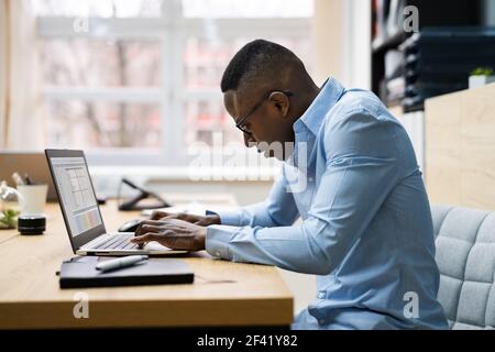 Uomo africano cattiva postura di lavoro digitando alla scrivania Foto Stock