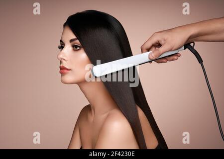 Parrucchiere la raddrizzatura lunghi capelli scuri con capelli ferri da stiro. Bella donna con lunghi capelli dritti. Capelli lisci Foto Stock