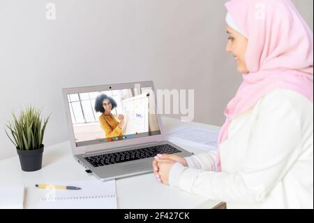 Due donne imprenditrici discutere di strategia di lavoro, piano per l'anno, guardando il reddito sul grafico, pc schermo vista sulla spalla islamica donna su una ragazza giovane con capelli ricci indossare occhiali Foto Stock