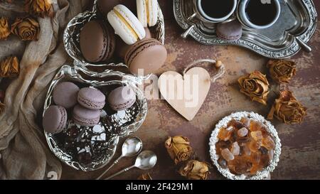 Un set di diversi macaron francesi per tè e caffè. Macaron al cioccolato e alla vaniglia con caffè e zucchero di caramello su un tavolo di legno. Vista dall'alto Foto Stock