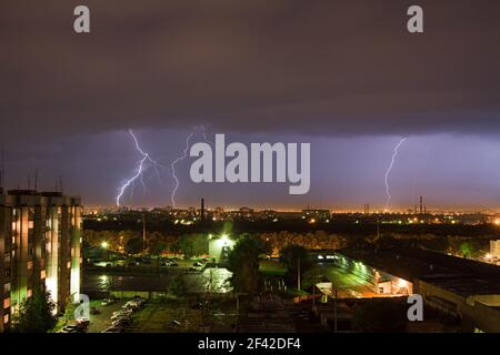 Il potente fulmine colpisce la città di notte. Un forte colpo di fulmine su un cielo grigio scuro colpisce la terra, illuminando la città. Foto Stock