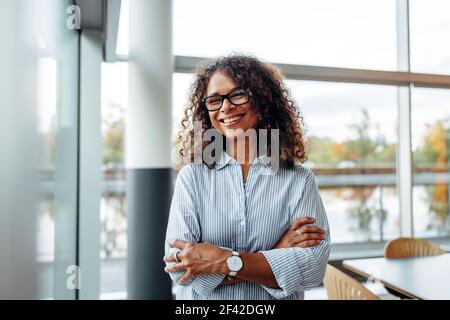 Ritratto di successo femminile professionista con le braccia incrociate. Donna d'affari sorridente in carica. Foto Stock