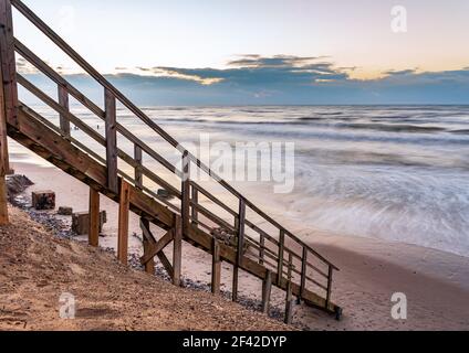 una scalinata in legno che permette di raggiungere la spiaggia molto vicina al litorale dell'acqua, proprio come entrare direttamente nell'acqua di mare Foto Stock