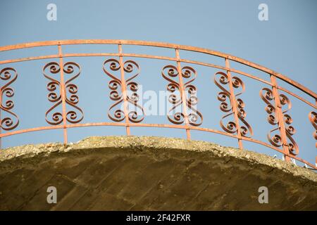 Moderno balcone rosso, recinzione in ferro battuto con forme cardiache contro il cielo blu, ringhiere, esterno di un edificio, pavimento incompiuto Foto Stock