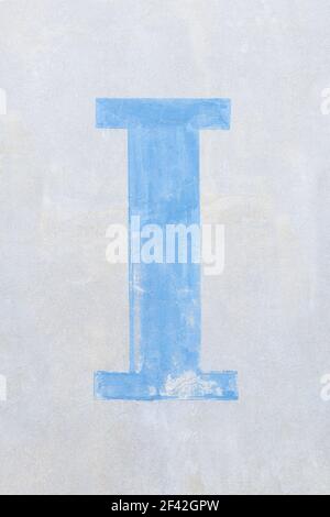 Lettera blu chiaro i(i) in carattere serif su una luce parete grigia Foto Stock