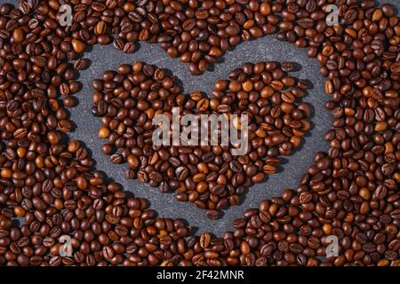 Chicchi di caffè marroni arrostiti su sfondo grigio. Modello per la pubblicità del caffè in forma cuore. Vista dall'alto. Foto Stock