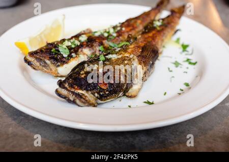 Due pesci di goda di mare fritti su piatto bianco con primo piano di limone. Cucina mediterranea, cibo spazzatura, gustosi spuntini per il concetto di birra Foto Stock