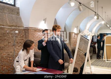 Adattare il vestito sul cliente vicino allo specchio e all'assistente Foto Stock