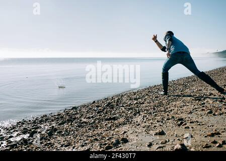uomo che schiava una pietra nell'oceano su un sole Giorno nel Regno Unito Foto Stock
