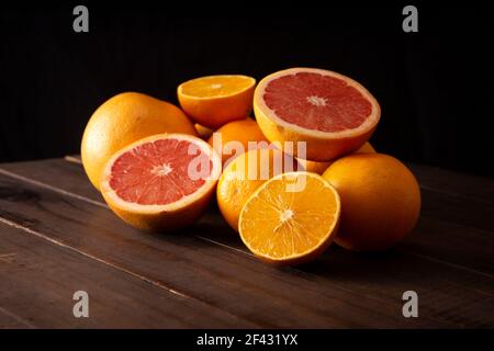 fette di arancia e pompelmo mature e diverse arance intere tavolo rustico marrone in legno Foto Stock