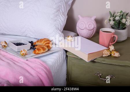 Domenica mattina prima colazione a letto con caffè, croissant, mirtilli e un libro in un ambiente romantico. Foto Stock