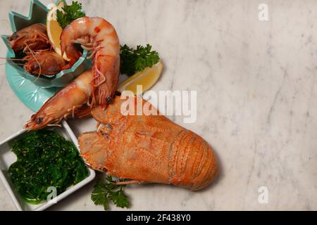 Una festa di pesce che include grandi gamberi del re in una ciotola, Moreton Bay Bug, un tipo di aragosta, e insalata di alghe su uno sfondo di marmo bianco e grigio. Foto Stock