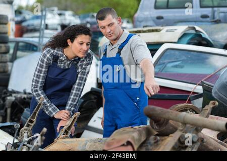 meccanico femminile che viene mostrato rottami auto in cantiere spazzatura Foto Stock