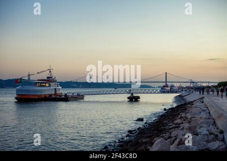 Un traghetto che aspetta i passeggeri prima di attraversare il fiume Tejo al tramonto, con il Ponte de 25 abril, visibile sullo sfondo, Lisbona, Portogallo. Foto Stock