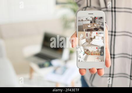 Donna che mostra telefono cellulare con immagini di telecamere cctv installate in appartamento su schermo, primo piano Foto Stock